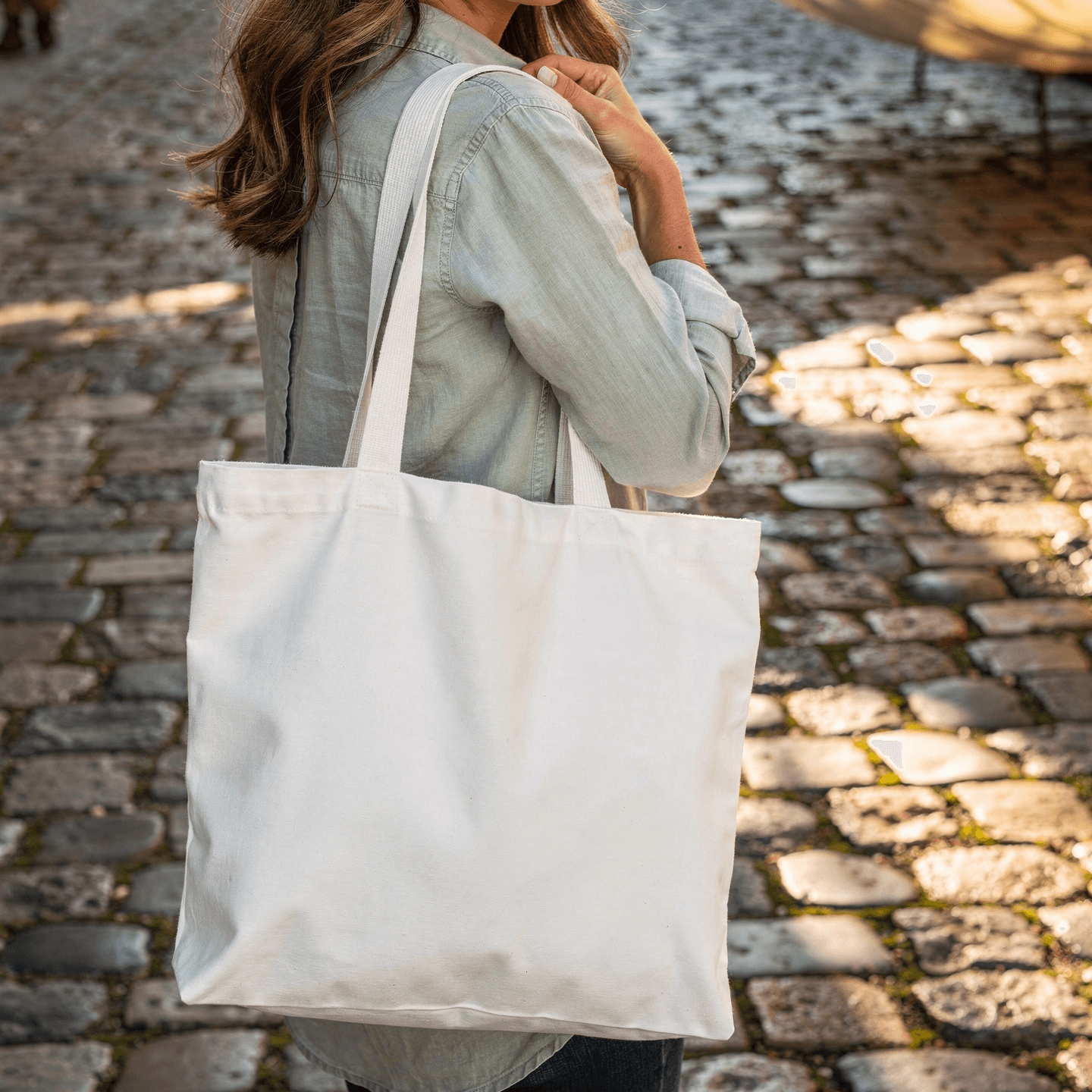 White Canvas Tote Bag Mockup - Cobblestone Setting — Hand-Held Casual Grip